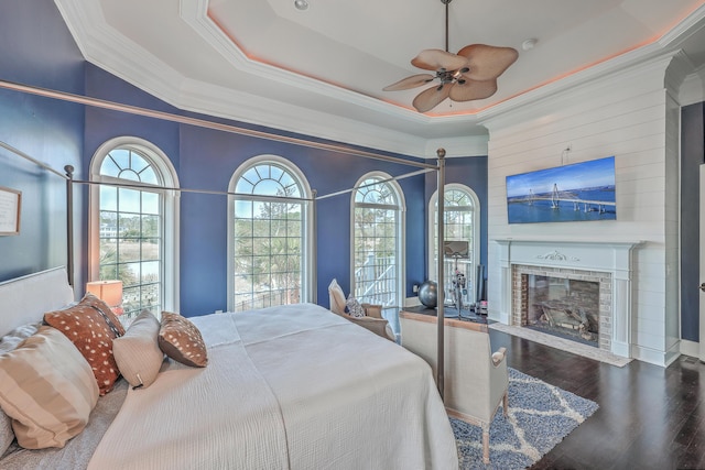 bedroom featuring a fireplace with flush hearth, wood finished floors, a ceiling fan, a raised ceiling, and crown molding