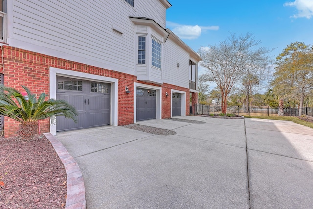 view of side of home featuring driveway, brick siding, an attached garage, and fence