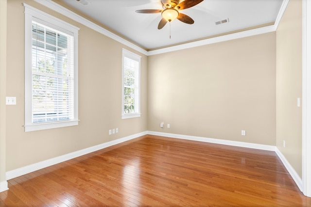 empty room with visible vents, hardwood / wood-style floors, ornamental molding, ceiling fan, and baseboards