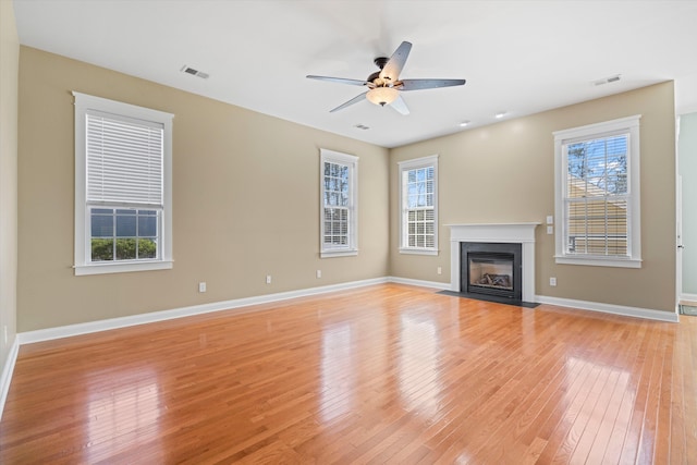 unfurnished living room featuring light wood-type flooring, a fireplace with flush hearth, visible vents, and baseboards