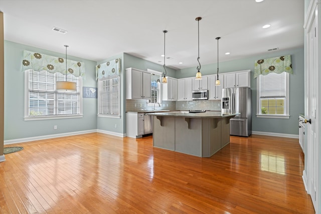 kitchen featuring a breakfast bar area, stainless steel appliances, a kitchen island, light wood-type flooring, and tasteful backsplash