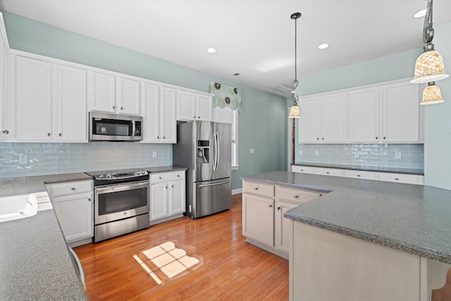 kitchen featuring light wood finished floors, hanging light fixtures, decorative backsplash, appliances with stainless steel finishes, and white cabinetry