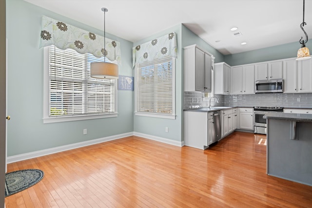 kitchen featuring stainless steel appliances, light wood finished floors, a sink, and decorative backsplash