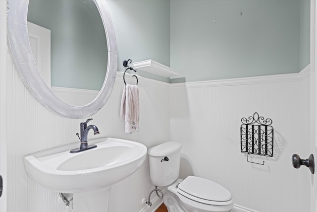 half bath with wainscoting, a sink, and toilet