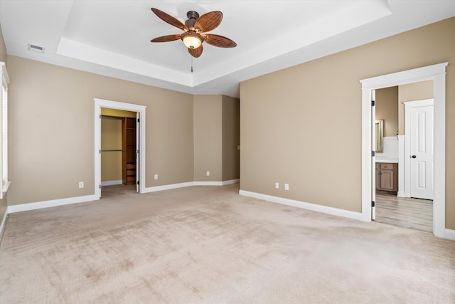 unfurnished bedroom featuring a tray ceiling, light colored carpet, and baseboards