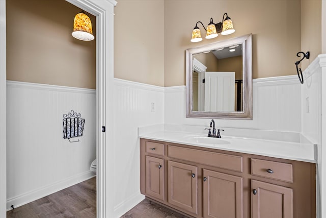 bathroom with a wainscoted wall, vanity, toilet, and wood finished floors