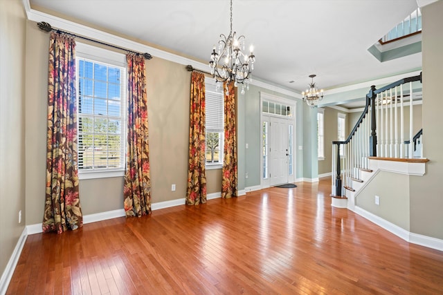 foyer entrance with crown molding, stairway, hardwood / wood-style flooring, and a notable chandelier