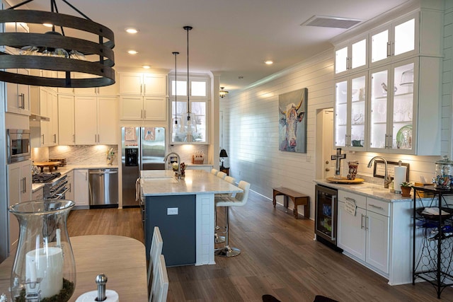 kitchen with light stone countertops, beverage cooler, appliances with stainless steel finishes, and dark wood finished floors