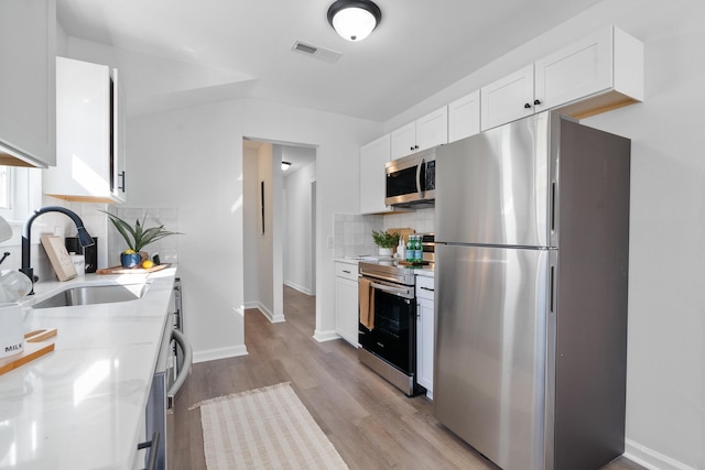 kitchen with appliances with stainless steel finishes, light stone counters, sink, white cabinetry, and tasteful backsplash