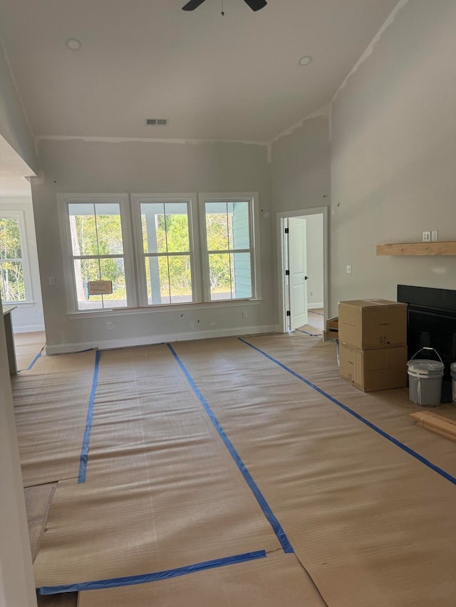 unfurnished living room featuring visible vents, baseboards, ceiling fan, a high ceiling, and a fireplace