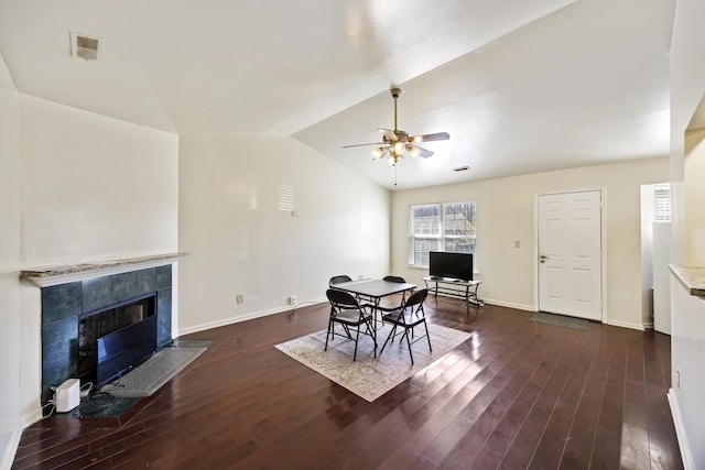 dining area with ceiling fan, dark hardwood / wood-style floors, lofted ceiling, and a tiled fireplace