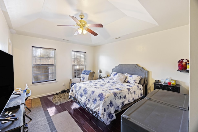 bedroom with ceiling fan, dark hardwood / wood-style floors, and a tray ceiling