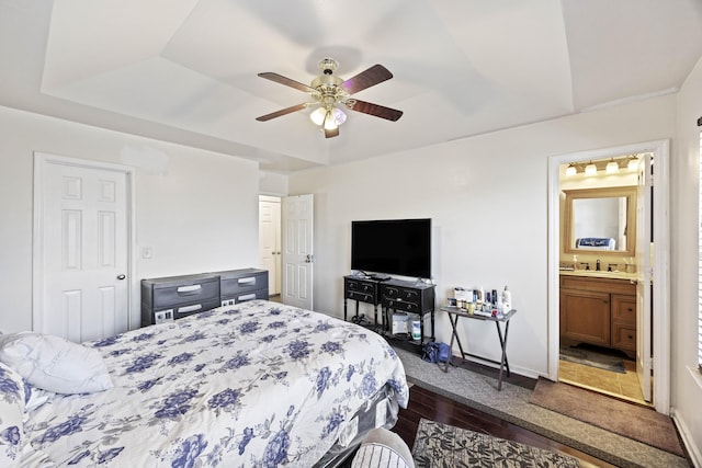 bedroom with ceiling fan, ensuite bathroom, a raised ceiling, sink, and dark wood-type flooring