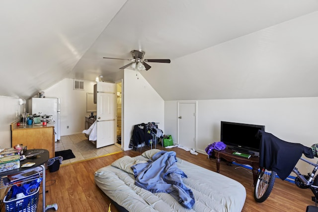 bedroom with ceiling fan, vaulted ceiling, white fridge, and light hardwood / wood-style floors