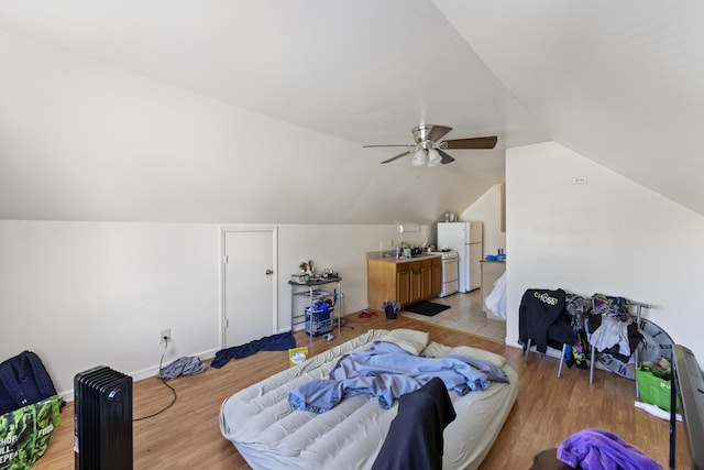 bedroom with ceiling fan, vaulted ceiling, white refrigerator, and light hardwood / wood-style flooring