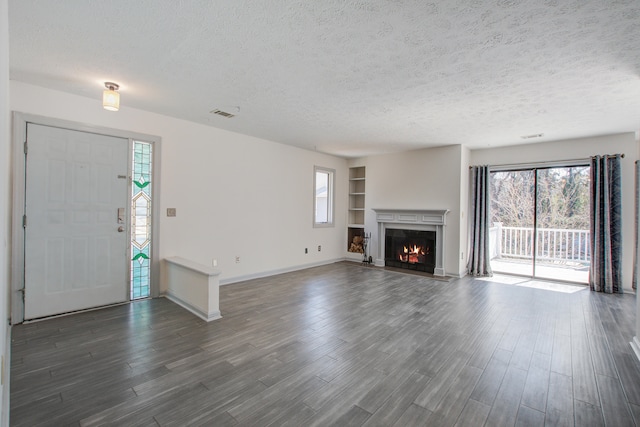 unfurnished living room featuring a wealth of natural light, a warm lit fireplace, a textured ceiling, and dark wood-type flooring