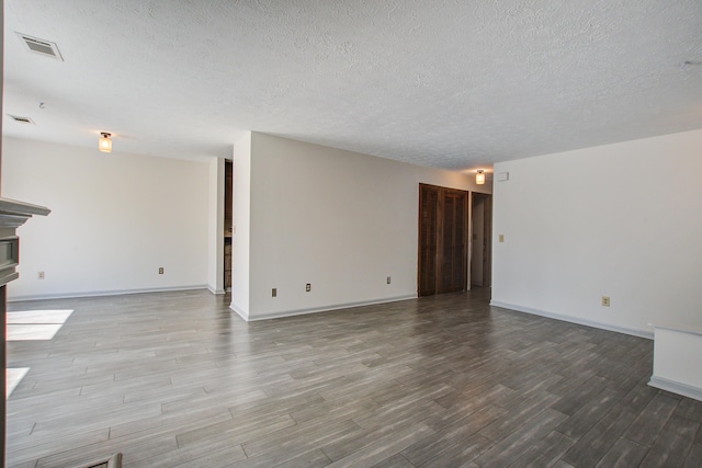 unfurnished room with a textured ceiling, wood finished floors, visible vents, and baseboards