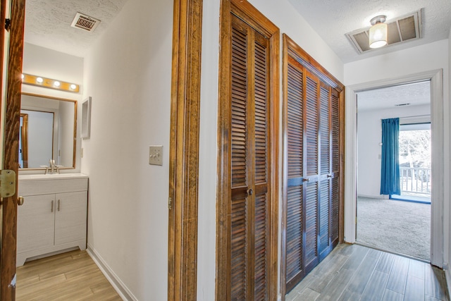 hallway with a textured ceiling, light wood-style flooring, a sink, visible vents, and baseboards