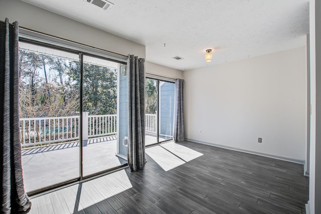 empty room featuring dark wood-style floors, visible vents, a textured ceiling, and baseboards