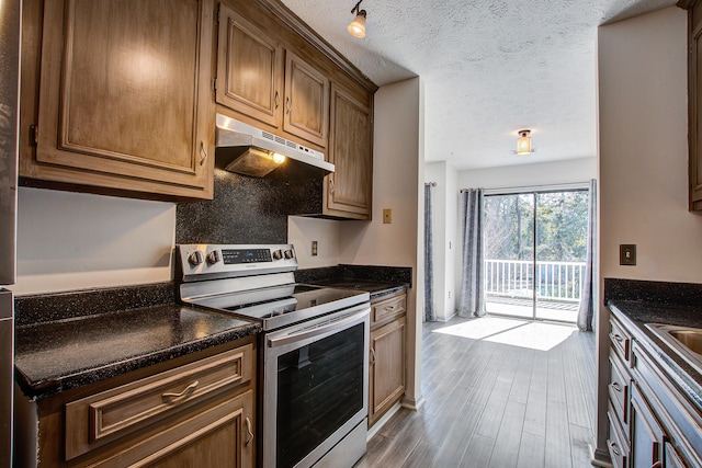 kitchen with electric stove, dark countertops, wood finished floors, a textured ceiling, and under cabinet range hood