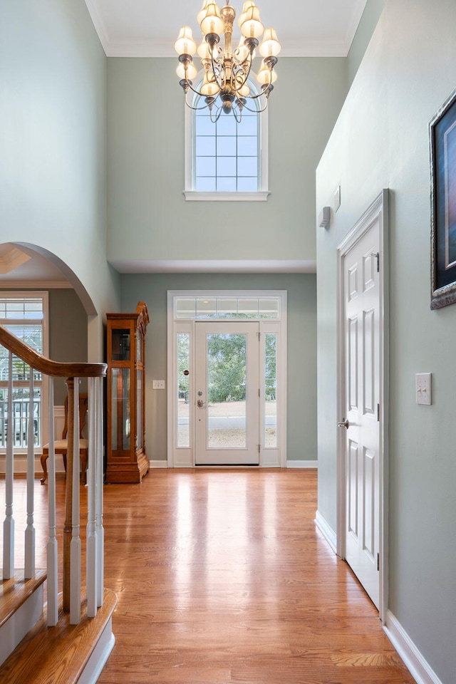 entryway with ornamental molding, a towering ceiling, a chandelier, and light hardwood / wood-style flooring