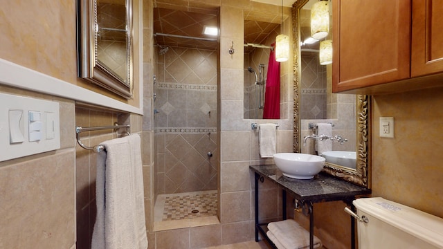 bathroom with toilet, a tile shower, vanity, and tile walls