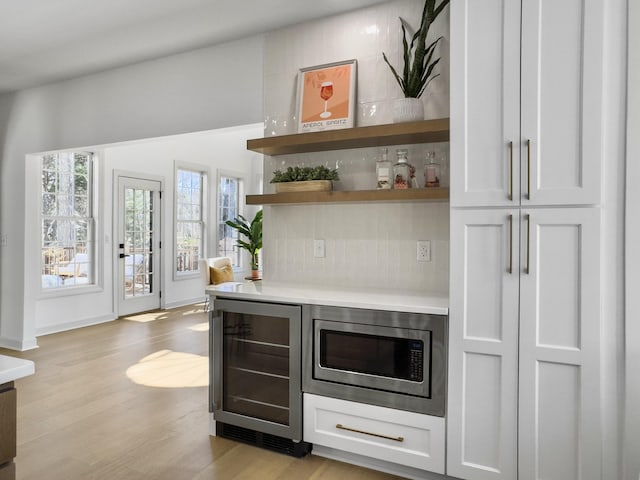 bar featuring stainless steel microwave, light wood-style flooring, a bar, beverage cooler, and baseboards