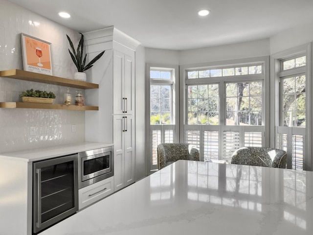 kitchen with open shelves, recessed lighting, stainless steel microwave, white cabinetry, and beverage cooler