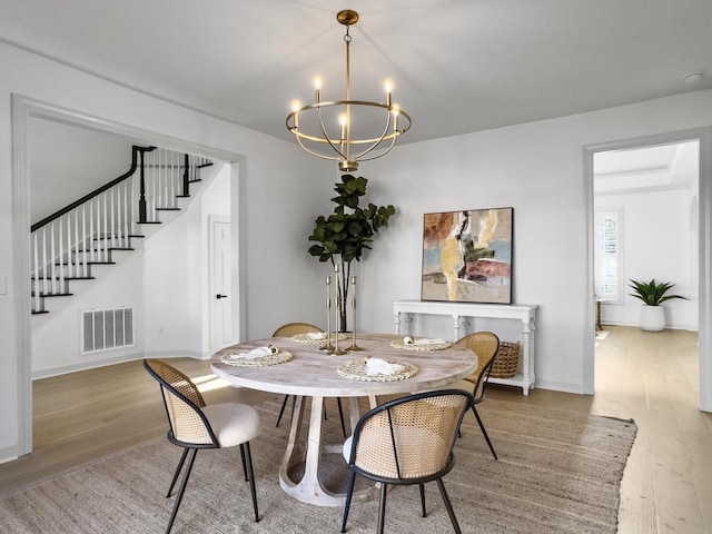 dining space with visible vents, baseboards, stairway, wood finished floors, and a notable chandelier