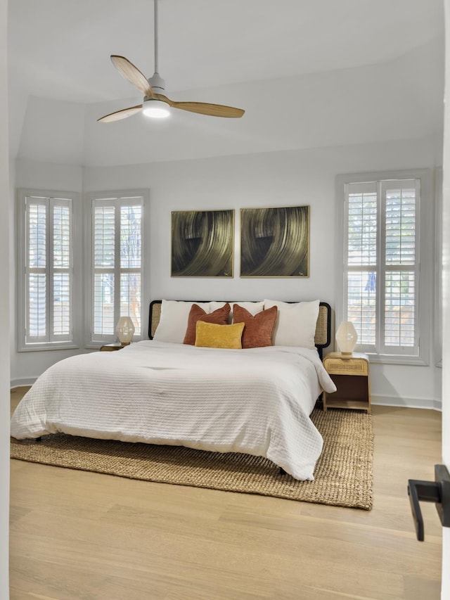 bedroom with a ceiling fan, multiple windows, baseboards, and wood finished floors