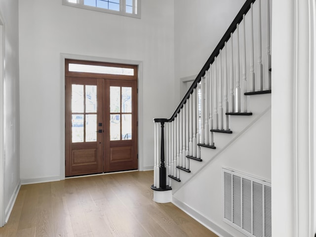 foyer entrance featuring a towering ceiling, baseboards, visible vents, and wood finished floors