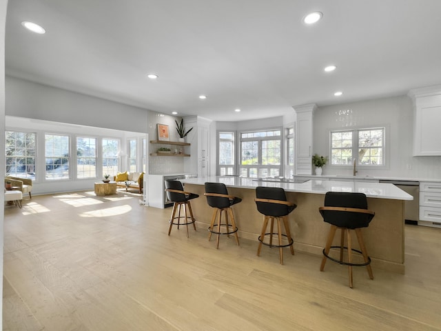 kitchen featuring dishwasher, a spacious island, light countertops, a healthy amount of sunlight, and a sink