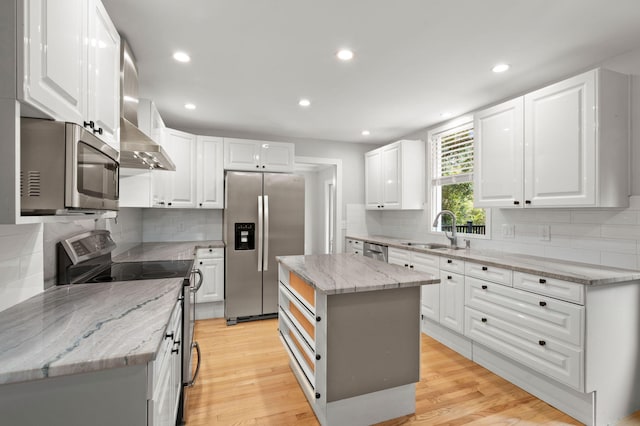 kitchen with light wood-type flooring, light stone countertops, appliances with stainless steel finishes, and a sink