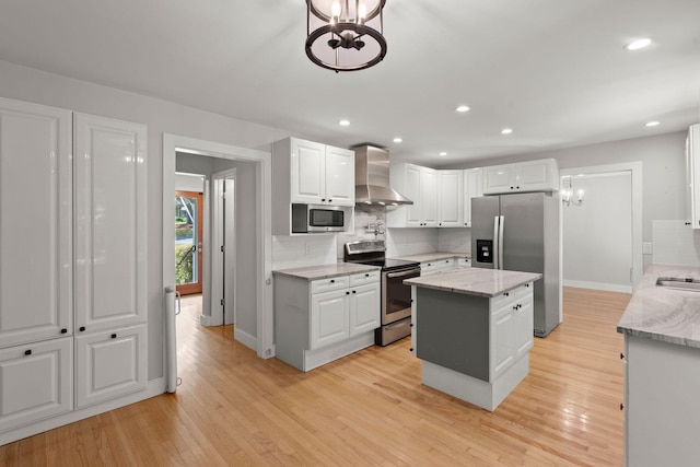 kitchen with a center island, stainless steel appliances, backsplash, light wood-style floors, and wall chimney exhaust hood