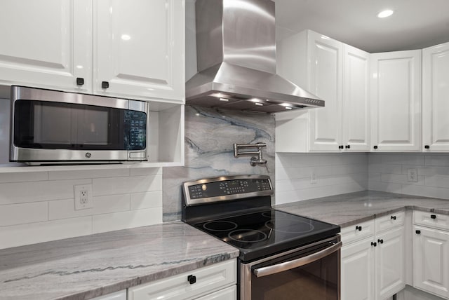 kitchen featuring wall chimney exhaust hood, appliances with stainless steel finishes, and white cabinets