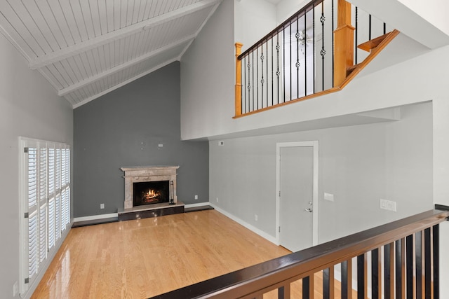 unfurnished living room featuring beam ceiling, a fireplace, wood finished floors, high vaulted ceiling, and baseboards