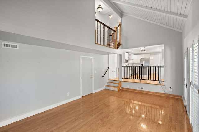 spare room featuring light wood-style flooring, visible vents, baseboards, stairway, and beam ceiling