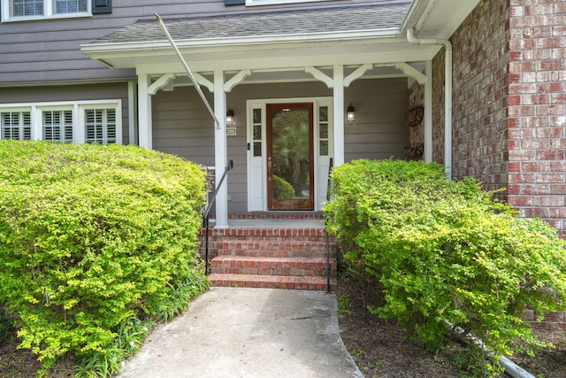 doorway to property with a porch, roof with shingles, and brick siding