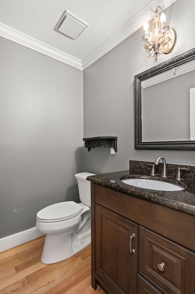 half bath with toilet, ornamental molding, vanity, wood finished floors, and baseboards