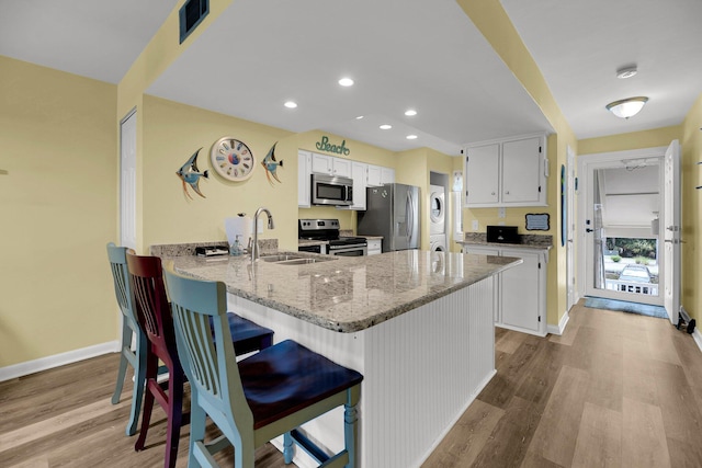 kitchen featuring appliances with stainless steel finishes, stacked washer / dryer, sink, white cabinets, and light stone countertops