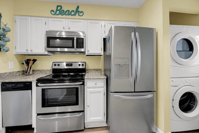 kitchen with light stone counters, stacked washer and dryer, appliances with stainless steel finishes, and white cabinets