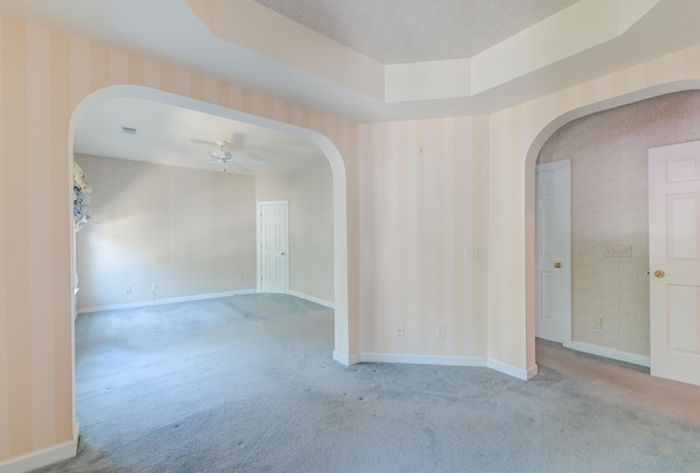 empty room with ceiling fan, light colored carpet, a textured ceiling, and a tray ceiling