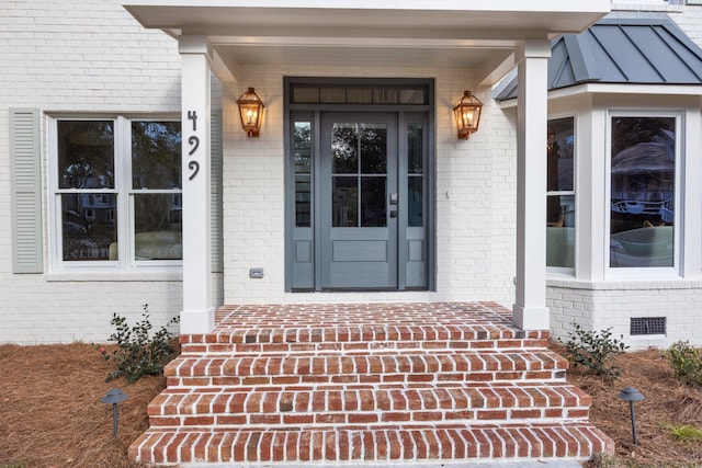 view of exterior entry with a standing seam roof, metal roof, brick siding, and crawl space