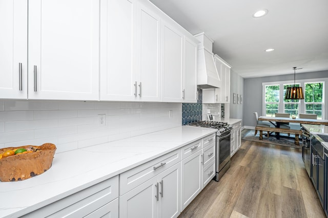 kitchen with stainless steel range with gas stovetop, white cabinets, recessed lighting, premium range hood, and wood finished floors