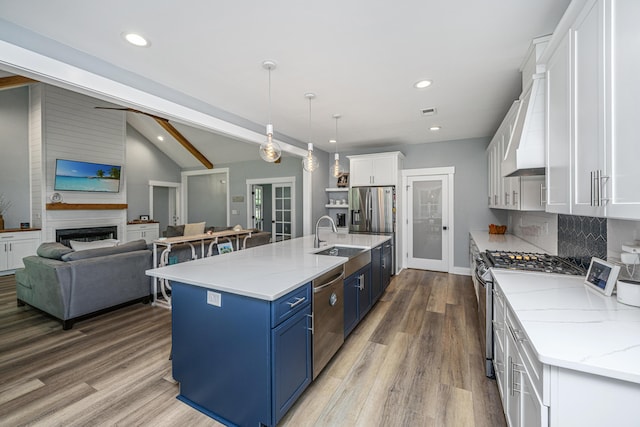 kitchen with blue cabinetry, appliances with stainless steel finishes, premium range hood, white cabinetry, and a sink