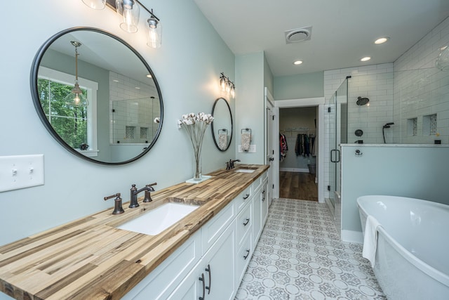 full bath featuring a shower stall, a soaking tub, double vanity, recessed lighting, and a spacious closet