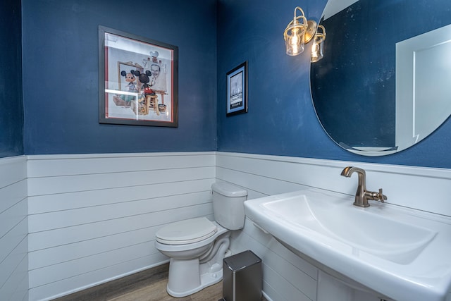 half bathroom with a wainscoted wall, a sink, toilet, and wood finished floors