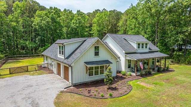 view of front of home with a porch, driveway, an attached garage, board and batten siding, and a wooded view
