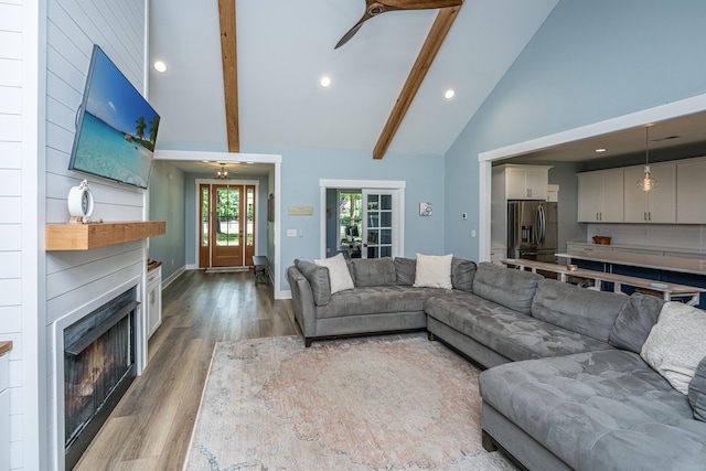 living area featuring wood finished floors, high vaulted ceiling, recessed lighting, beamed ceiling, and a lit fireplace