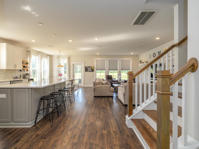 kitchen with tasteful backsplash, dark wood-type flooring, white cabinetry, hanging light fixtures, and a breakfast bar area